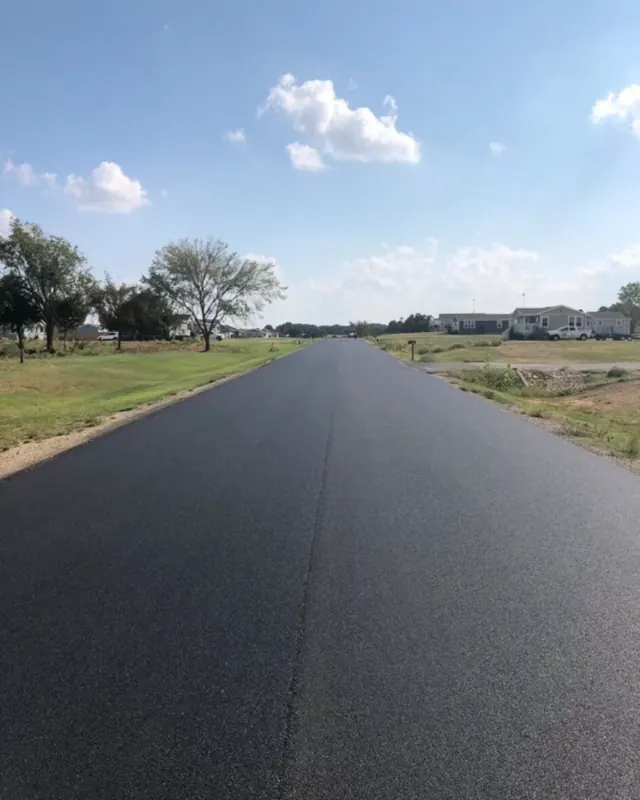 Long, freshly paved asphalt road through an open neighborhood
